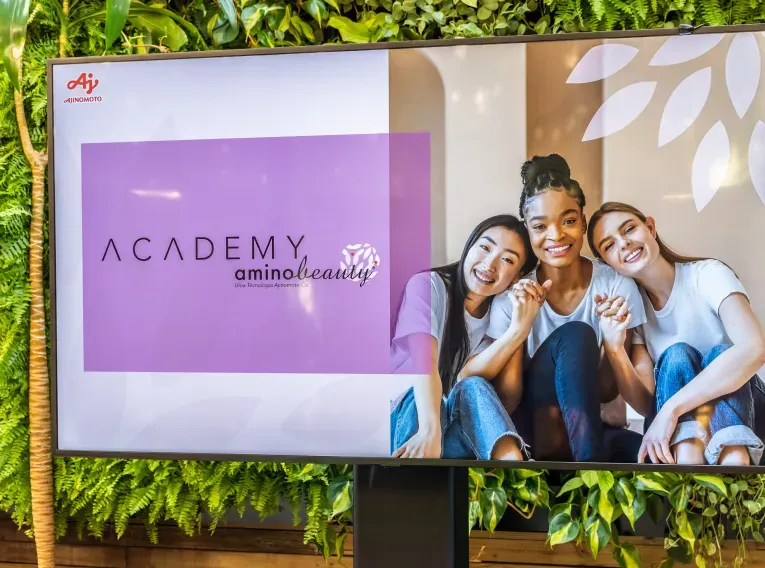 Uma televisão mostrando três mulheres e o logo 'Academy Aminobeauty' 