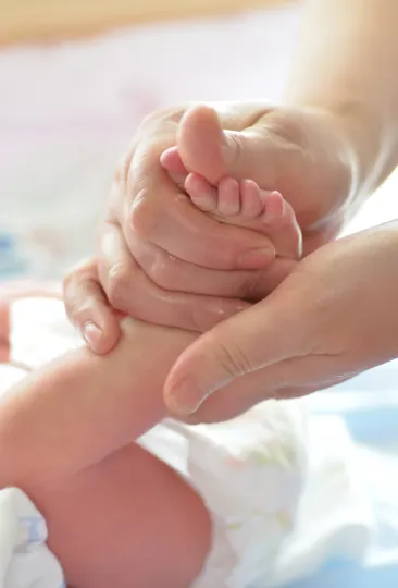 Uma mão adulta segurando gentilmente o pezinho de um bebê.