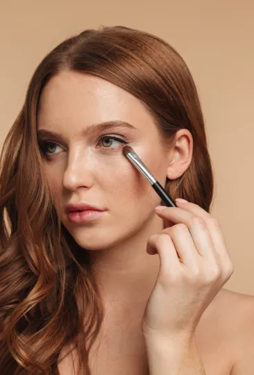 Uma mulher aplicando sombra nos olhos com um pincel.